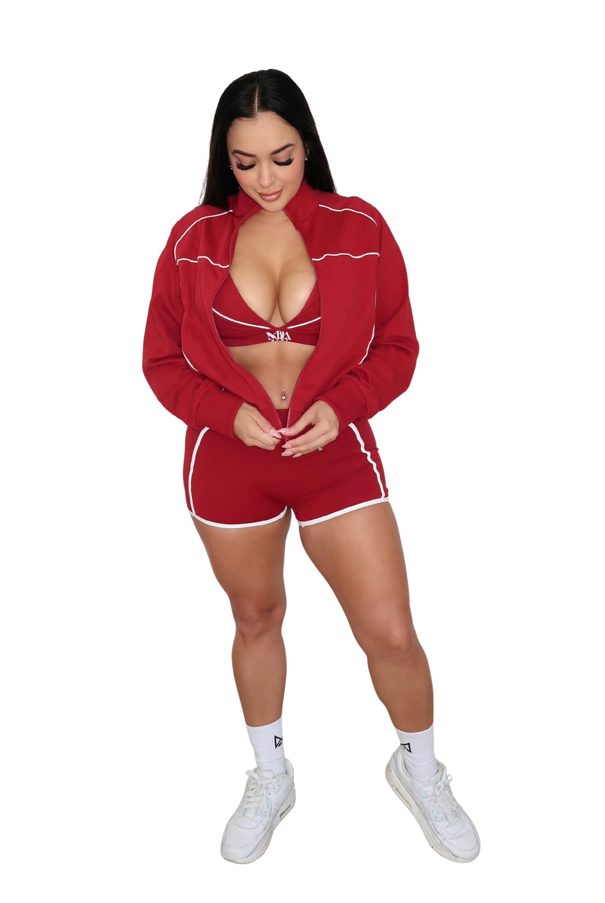 Woman wearing a red athletic outfit with a jacket, sports bra, and shorts on a white background