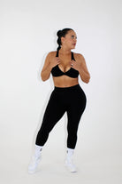 Woman wearing black leggings and a black sports bra - front view