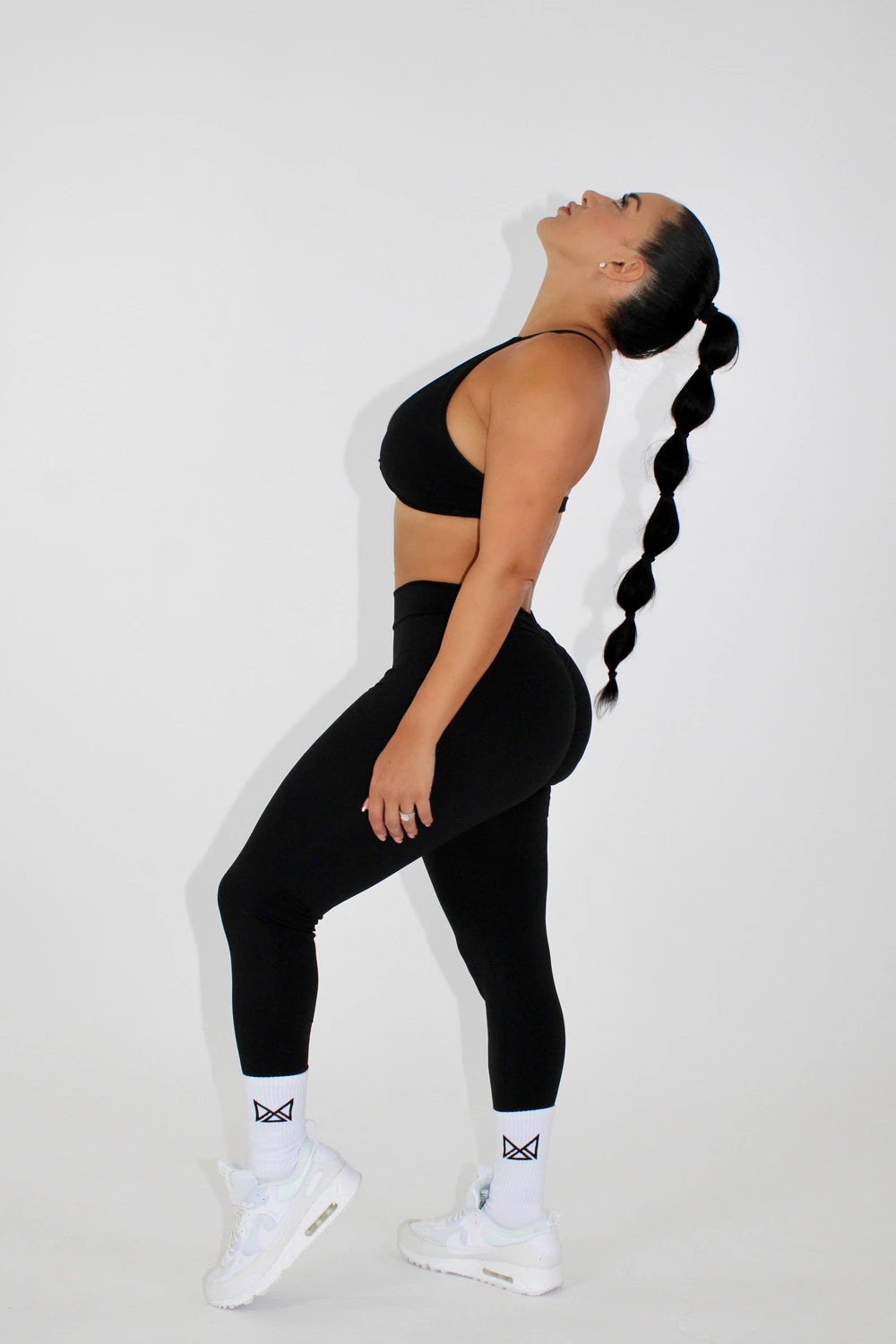 Woman wearing black leggings and a black sports bra - tilting head back side view